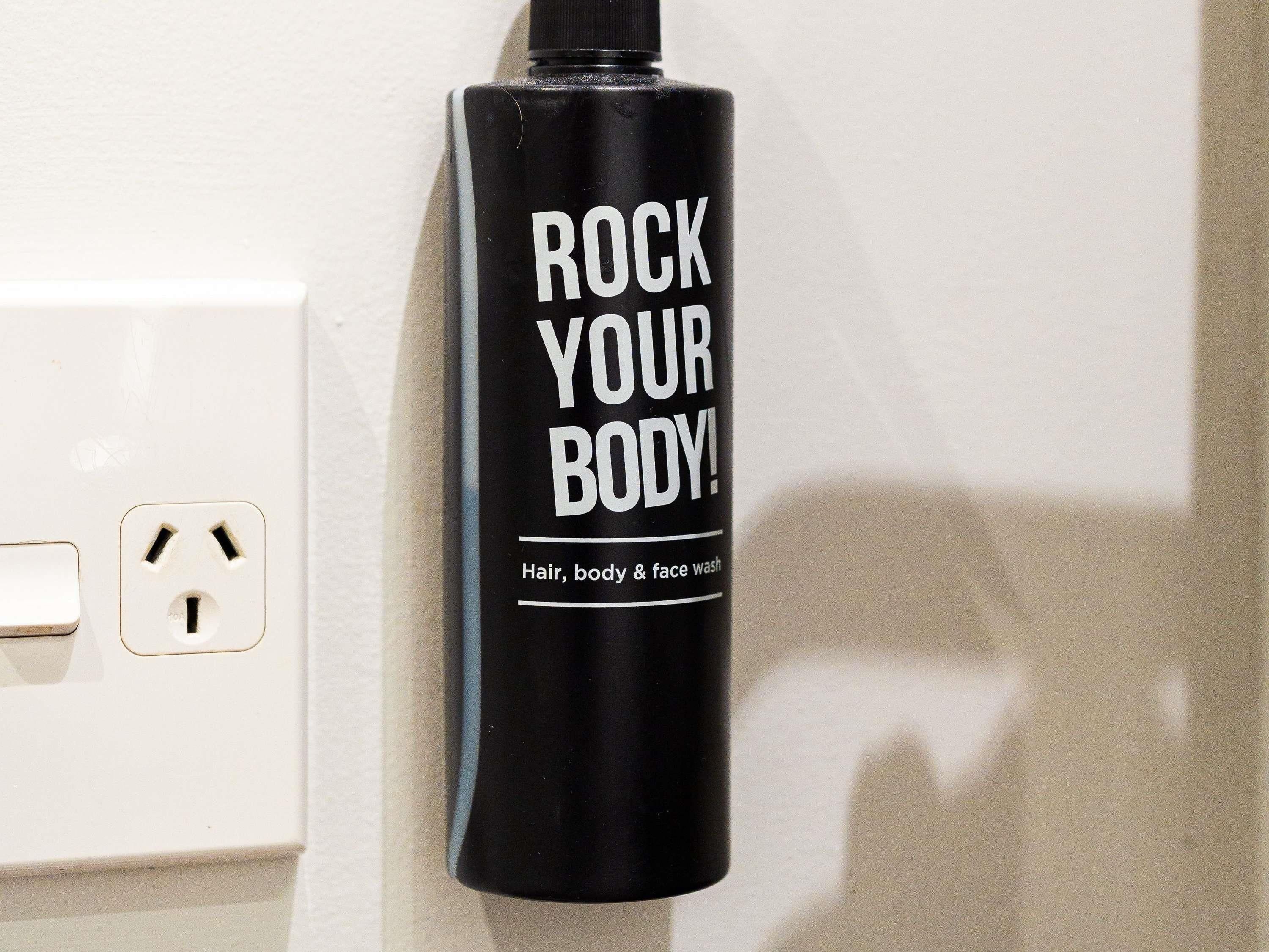 A black bottle with white text 'ROCK YOUR BODY!' and a label indicating it's for hair, body, and face wash.
