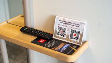 A wooden table with a remote control and a QR code sign for hotel services.
