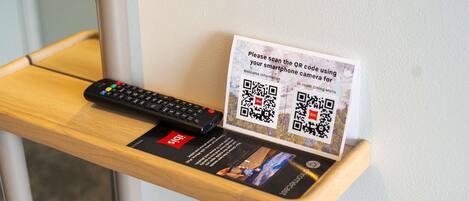 Una mesa de madera con un control remoto y un cartel con un código QR para servicios del hotel.