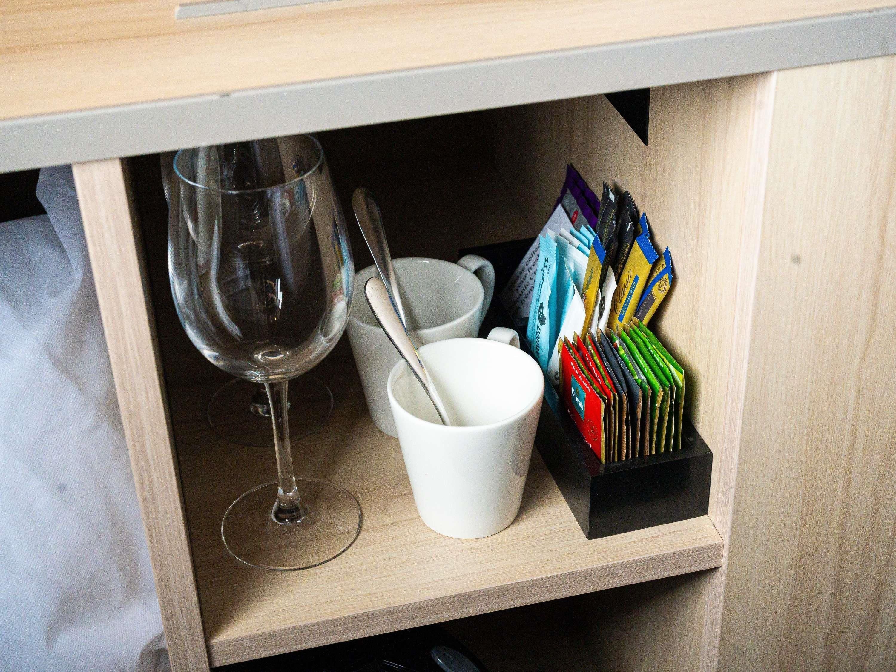 A wooden shelf with a wine glass, a white cup, and a cardholder.