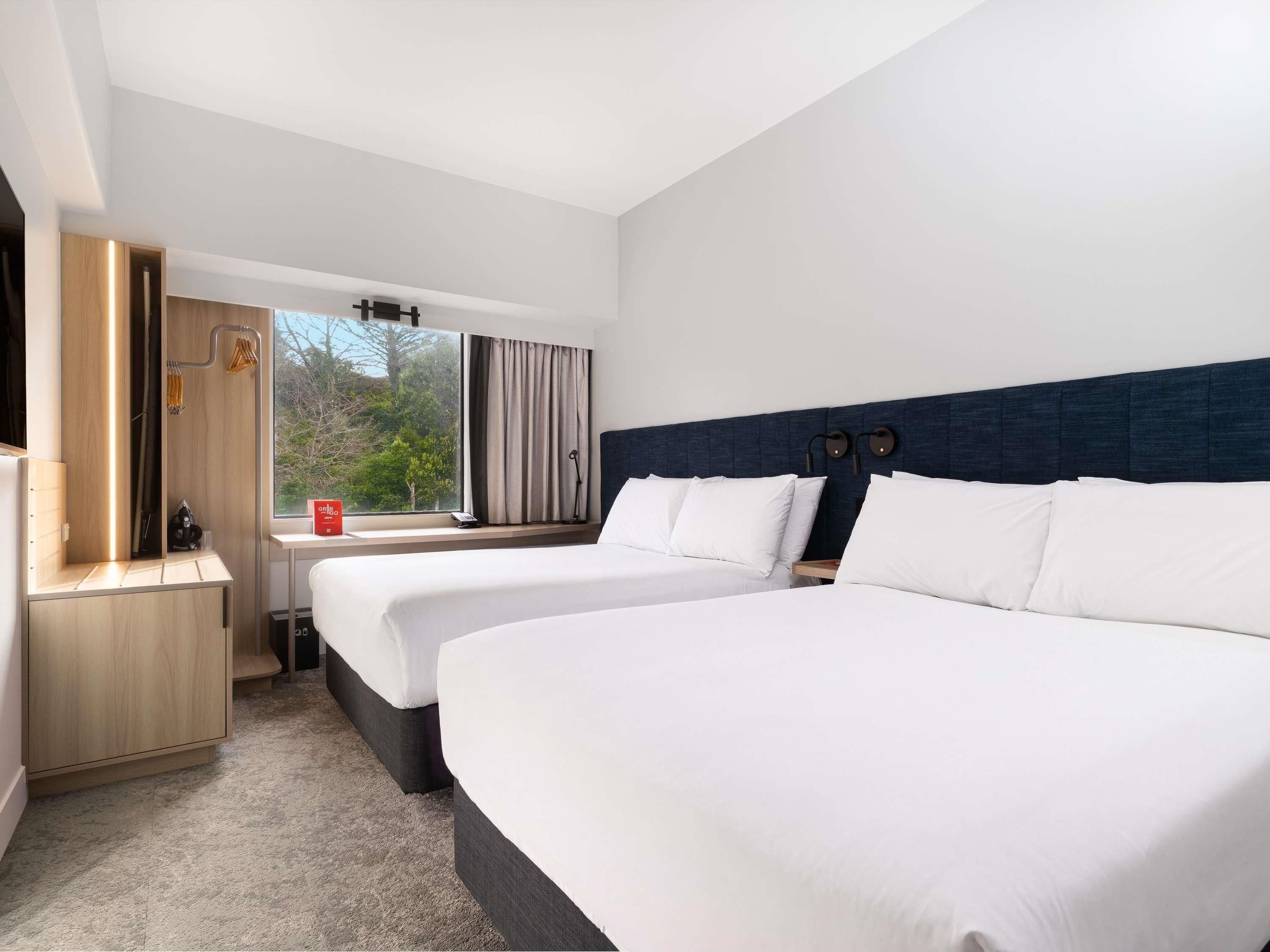 A hotel room with two beds, a desk, a chair, a wardrobe, and a window with curtains.