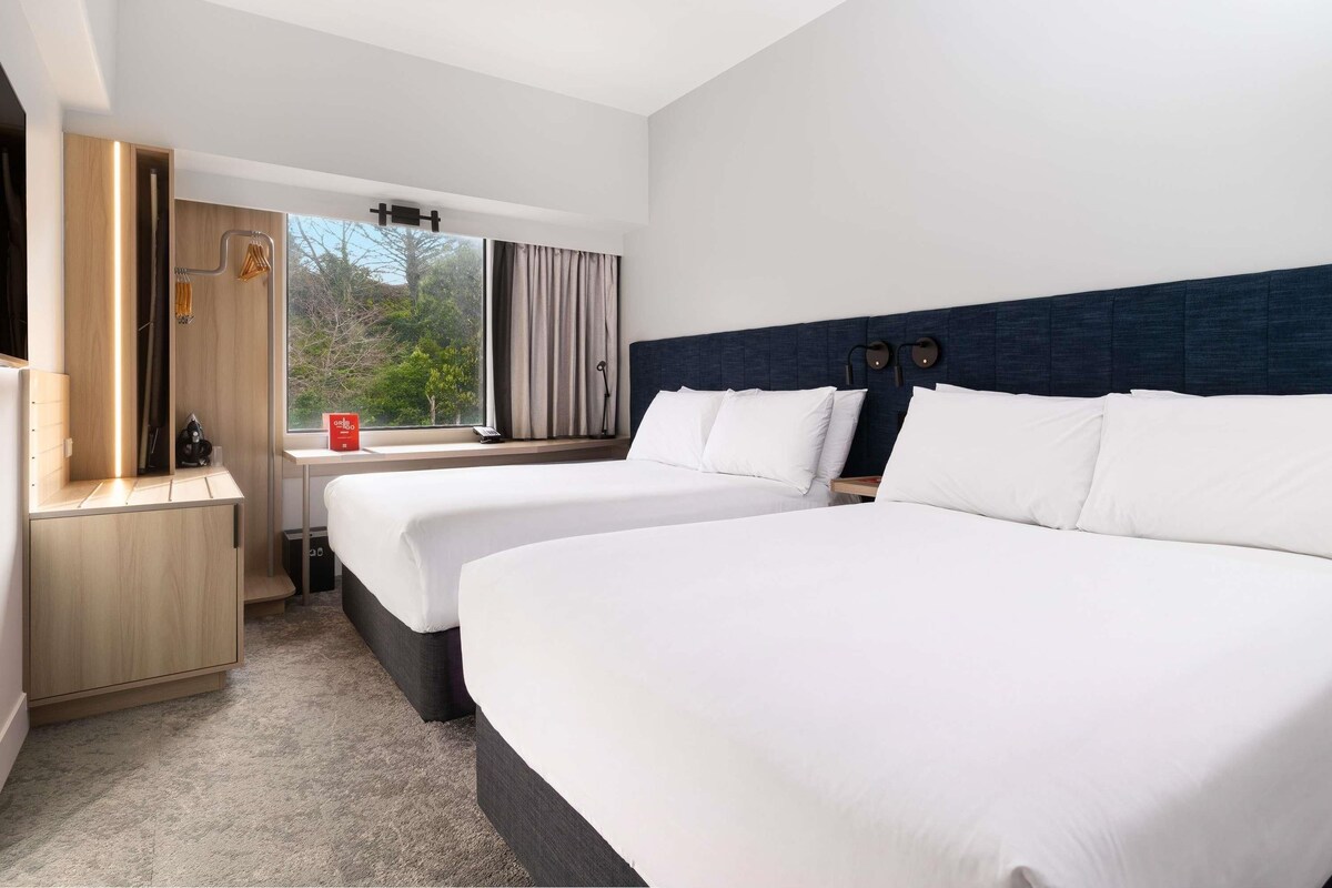 Habitación de hotel con dos camas, un escritorio, una silla, un armario y una ventana con cortinas.