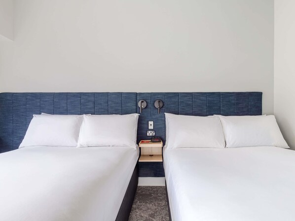 Una cama doble con cabecera azul, dos mesitas de noche y un reloj.