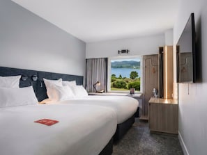 A hotel room with two beds, a large window with a view of the countryside, a flat-screen TV, and a wooden cabinet.