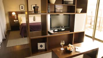 A hotel room with a bed, a TV, a coffee table with a glass of wine, and a bookshelf.