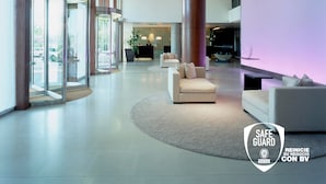 Een moderne lobby met een receptiebalie, een zithoek en grote glazen deuren die naar buiten leiden.