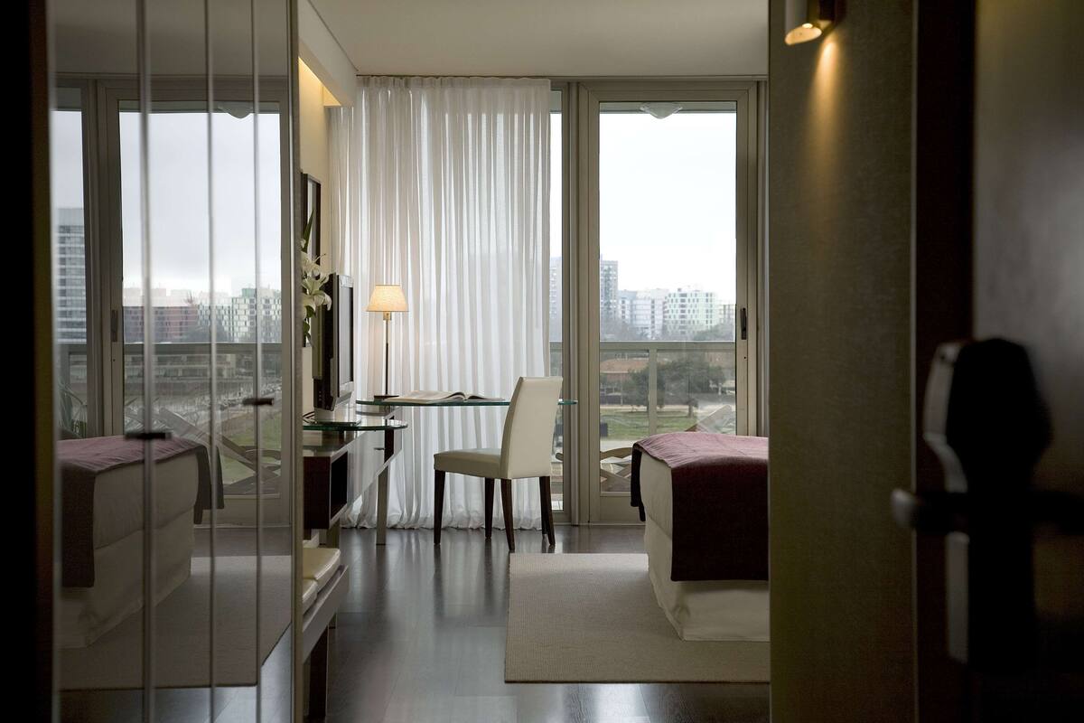 Una habitación de hotel moderna con un ventanal grande, un escritorio, una silla y una cama.