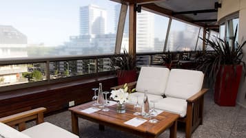 A balcony with a wooden table, white chairs, and potted plants.
