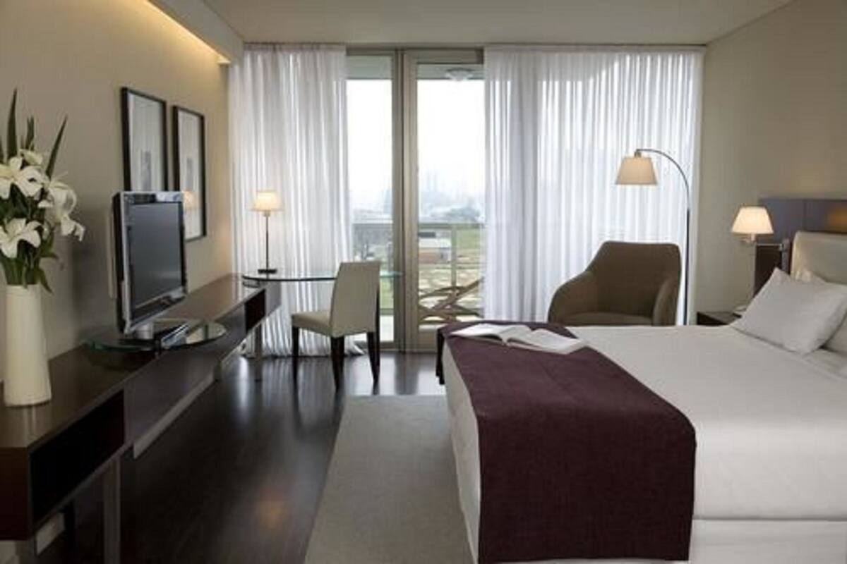 Habitación de hotel con cama, escritorio con televisor, una silla y vista por la ventana.
