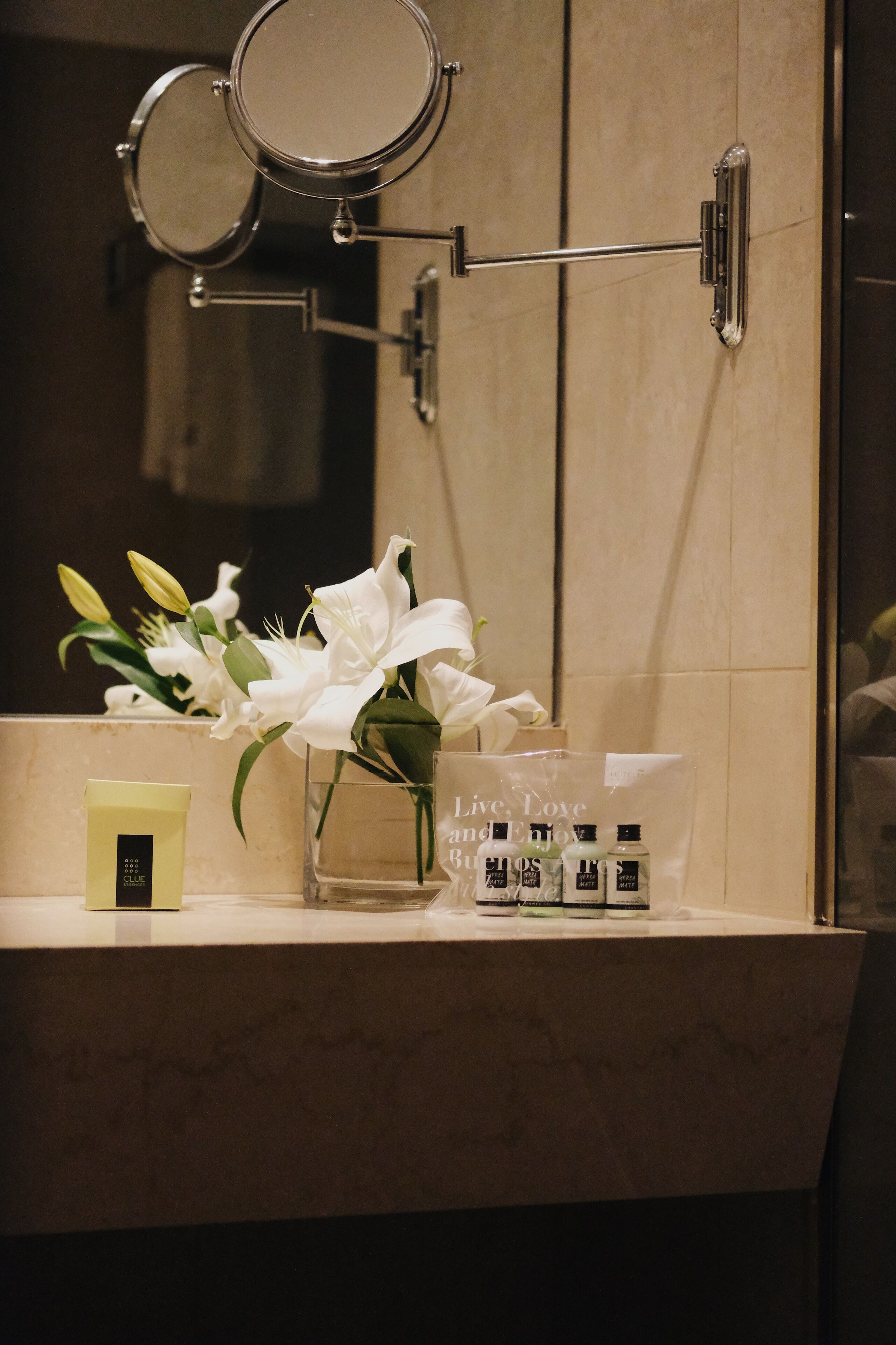 Een badkamermeubel met een spiegel, een vaas met witte bloemen en toiletartikelen.