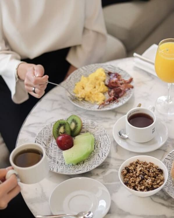Une table mise pour le petit-déjeuner avec des assiettes remplies de nourriture, une tasse de café, un verre de jus d’orange et un bol de granola.