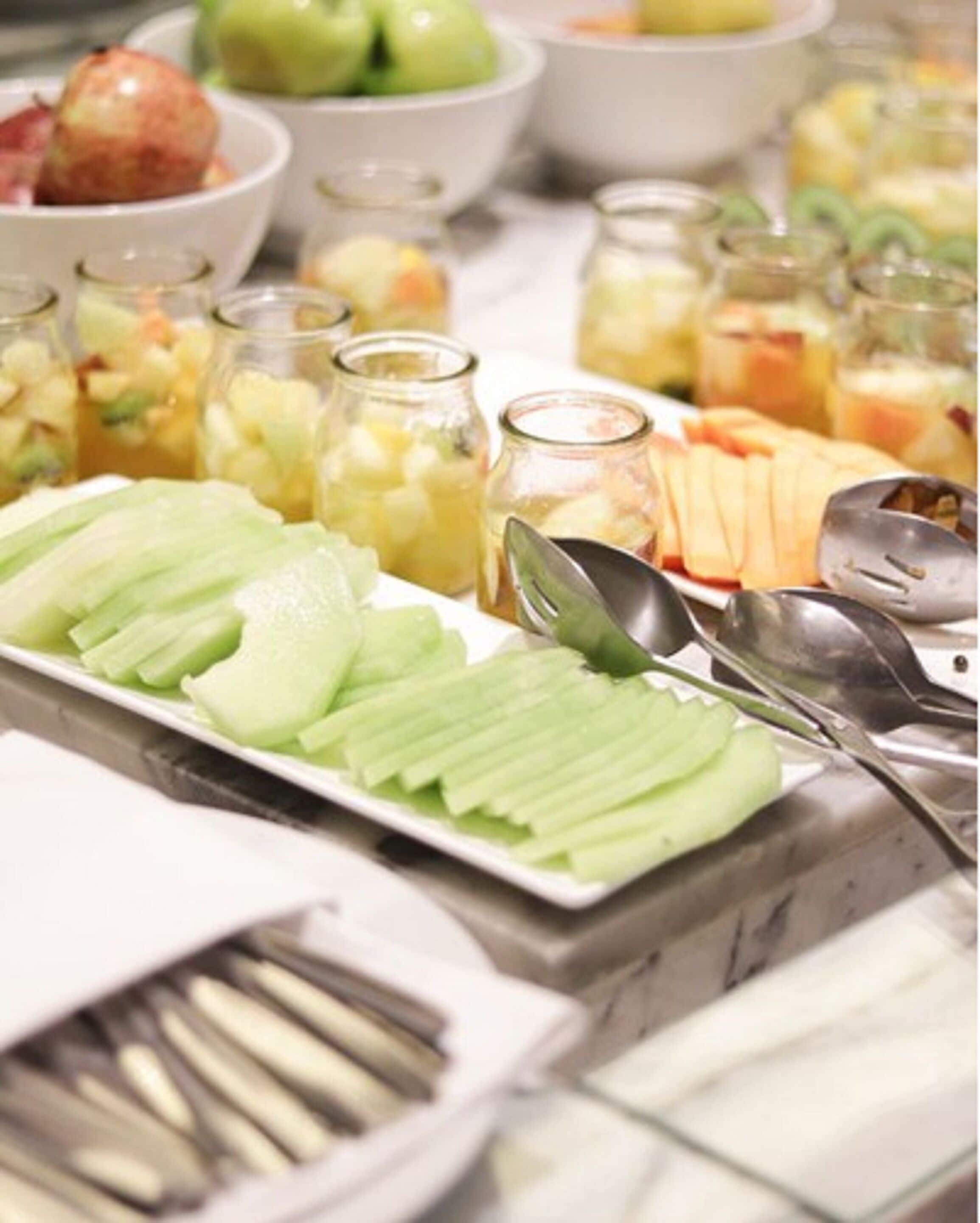 Un bufé con frutas y verduras diversas, incluyendo manzanas en rodajas y una variedad de otros platos en cuencos y frascos.