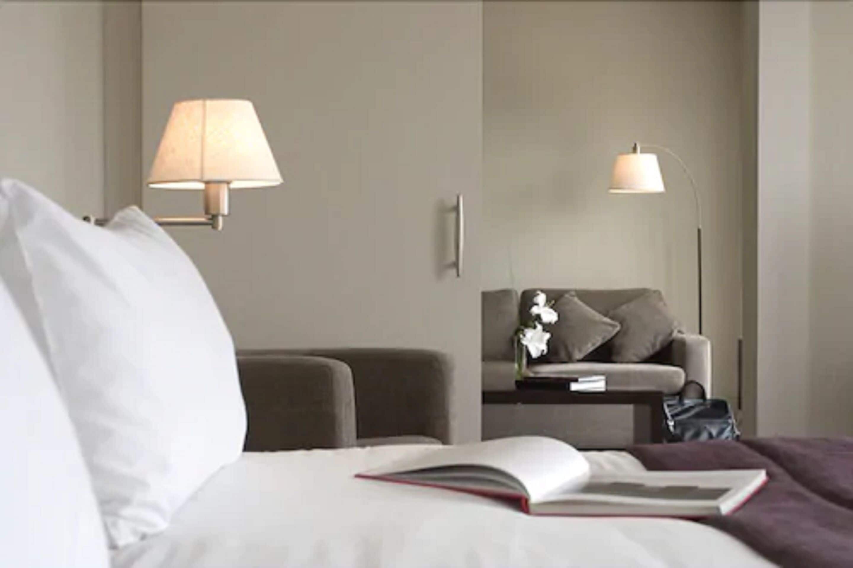 A hotel room with a bed, a nightstand, a lamp, a chair, and a small table with a vase of flowers.