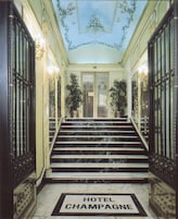 A grand hotel entrance with marble steps, a chandelier, and a ceiling with floral designs.