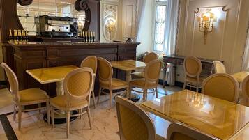 Un espace repas doté d’un sol en marbre, de tables et de chaises en bois. On y trouve également un bar avec une machine à café et des bouteilles.