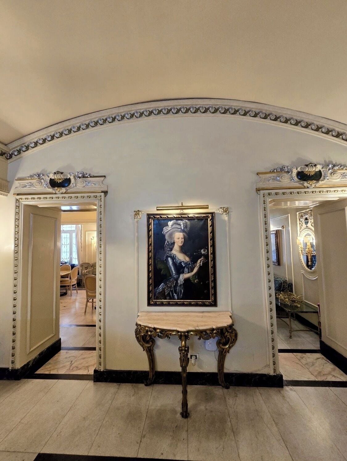 A hallway with ornate mirrors, a classical painting, and a marble floor.
