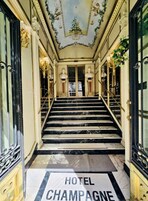 A grand hotel entrance with marble stairs, ornate ceiling decorations, and classical busts.