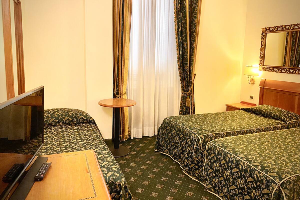 Une chambre d’hôtel avec deux lits, une petite table, une chaise, un miroir et un téléviseur.