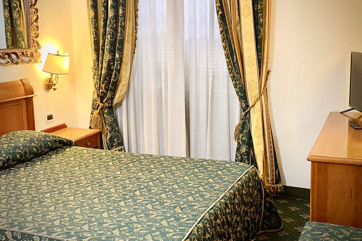 Une chambre d’hôtel avec un grand lit, une table de chevet, une lampe, une télévision et des rideaux.
