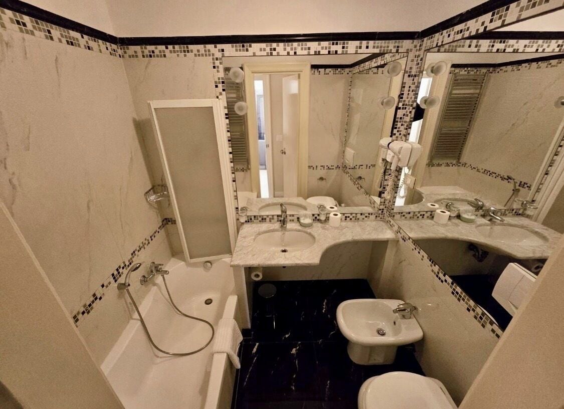 Een kleine badkamer met een bad, een bidet, een toilet en een spiegel.
