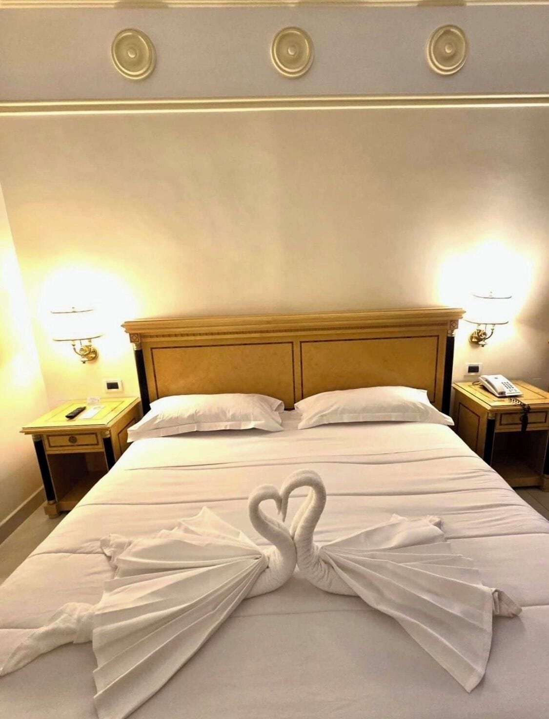 A hotel room with a large bed, two bedside tables with lamps, and a wall-mounted telephone.