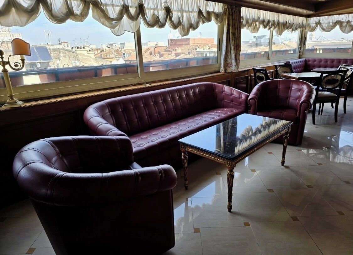 A room with a leather sofa, a glass coffee table, and a view of the cityscape through large windows.