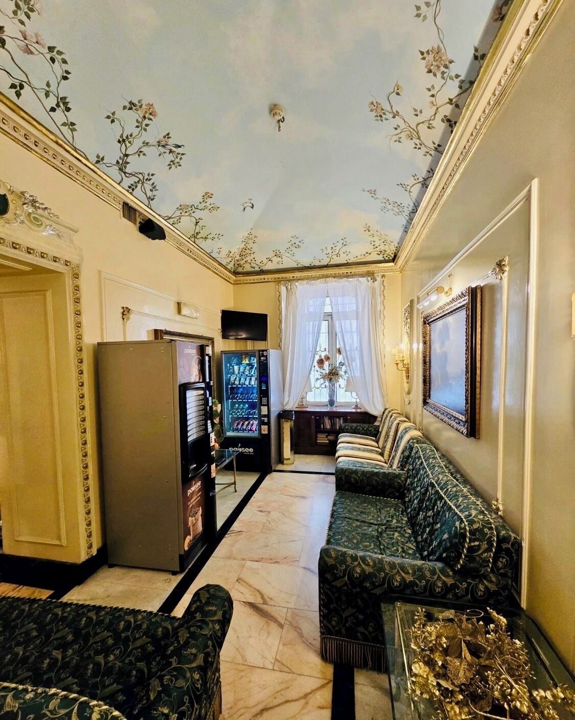 A room with a sofa, a television, a vending machine, and a decorative ceiling.