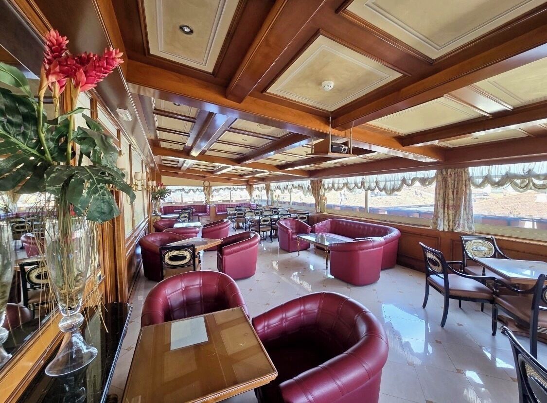 Um restaurante com vigas de madeira no teto, assentos em couro vermelho e grandes janelas.