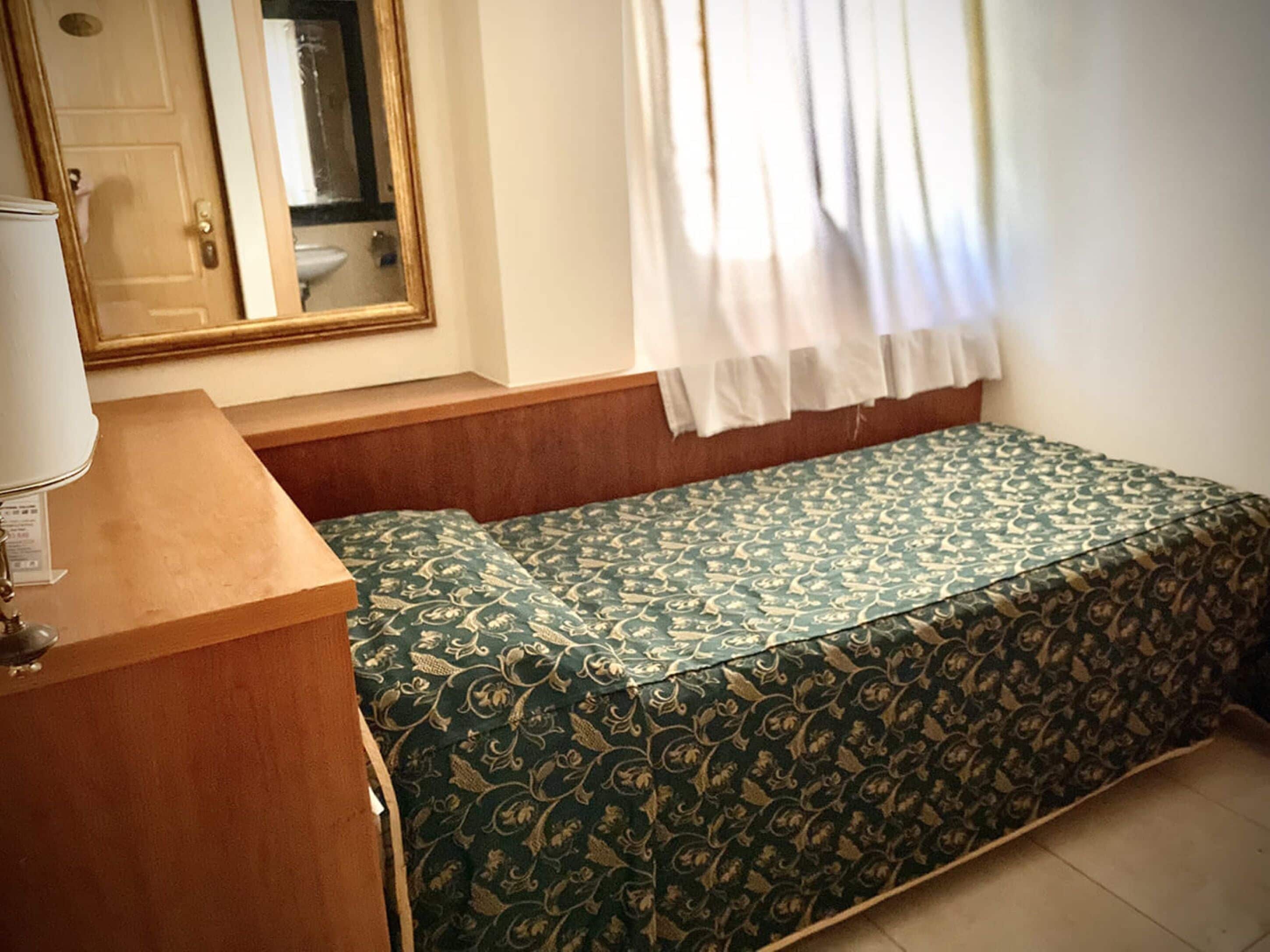 Una habitación con cama, una mesita, un espejo y una ventana con cortinas.