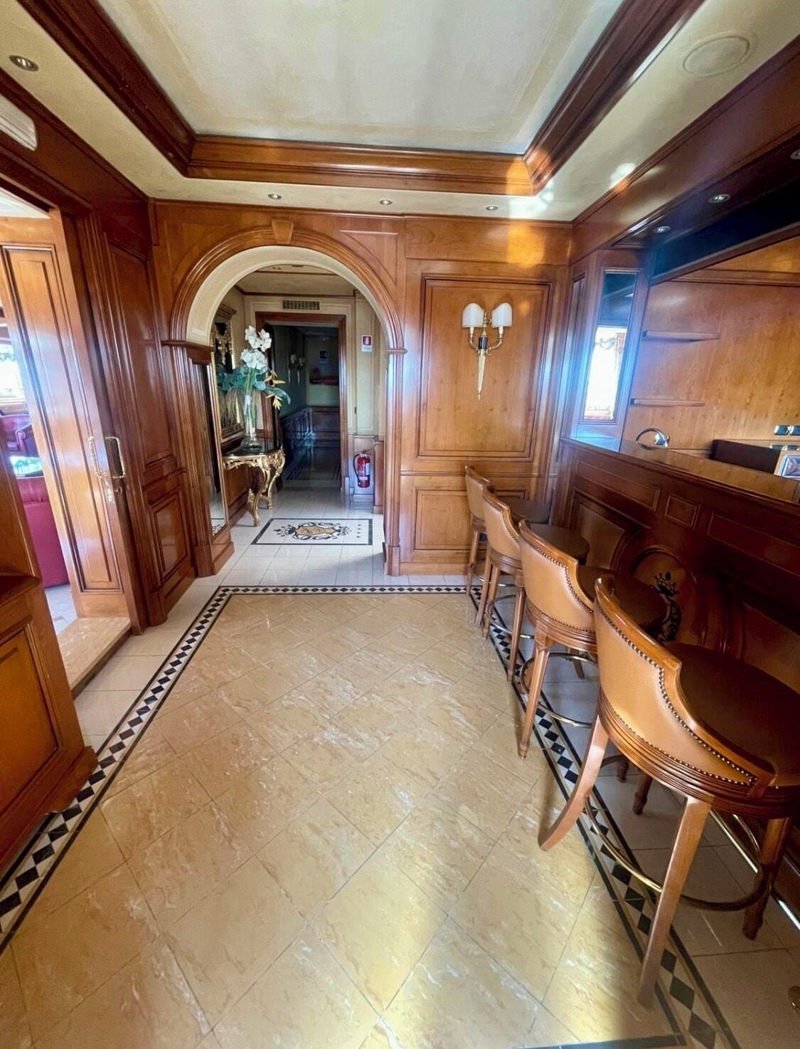 Un pasillo con paneles de madera, suelo de baldosas y una zona de estar con sillas y una mesa.