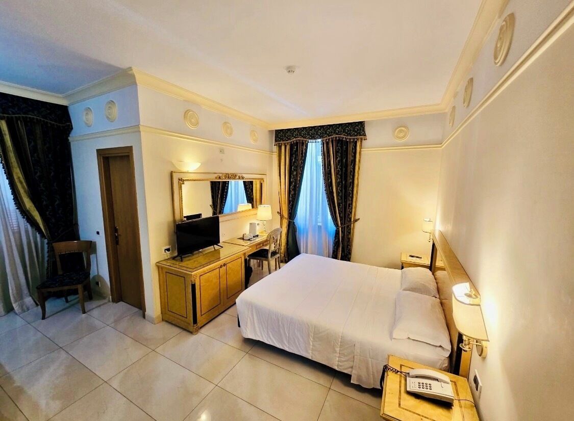 A hotel room with a bed, a desk with a computer, a television, and a telephone.