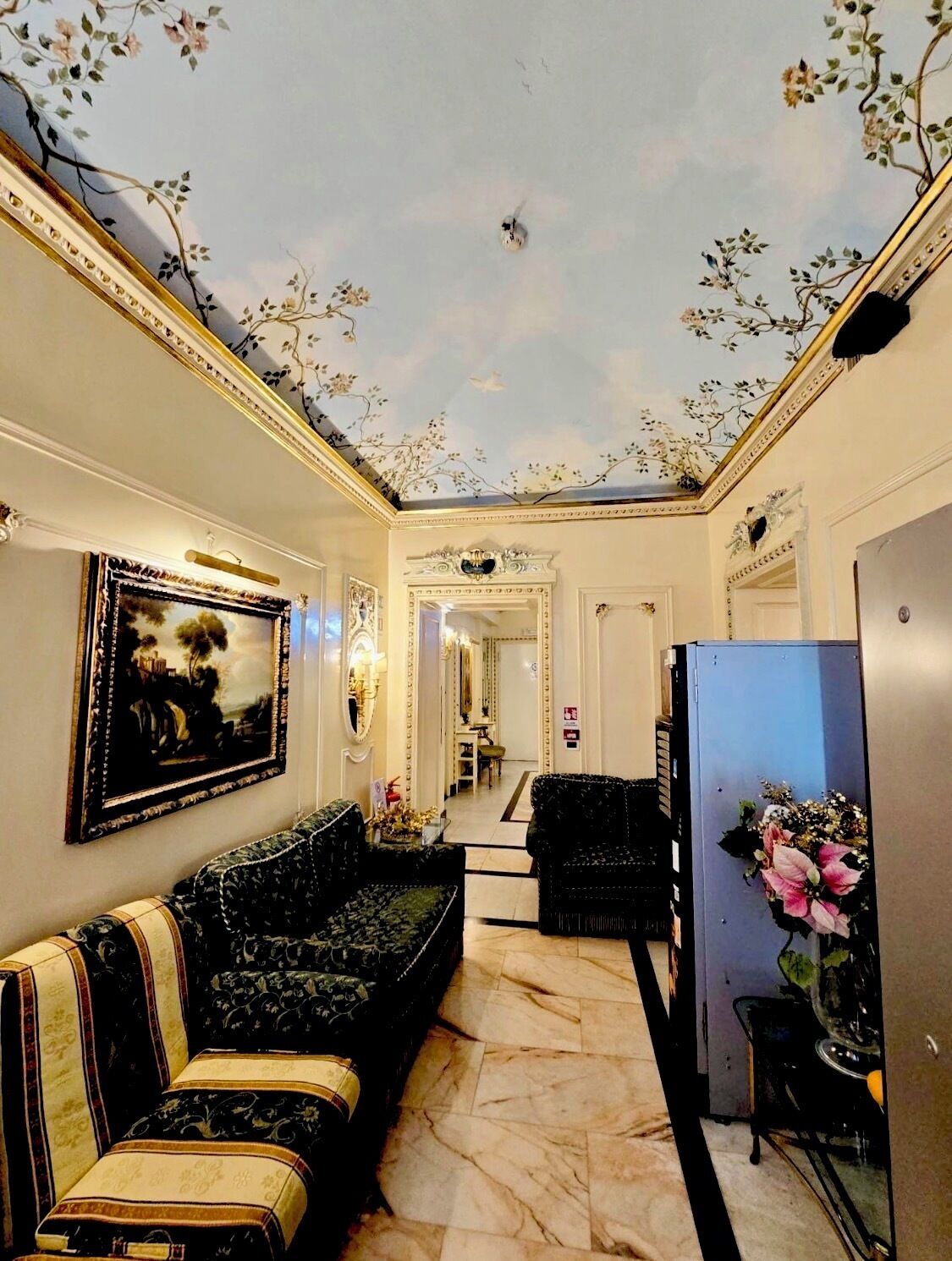 Un elegante ingresso con un affresco al soffitto, arredi raffinati e un moderno frigorifero.