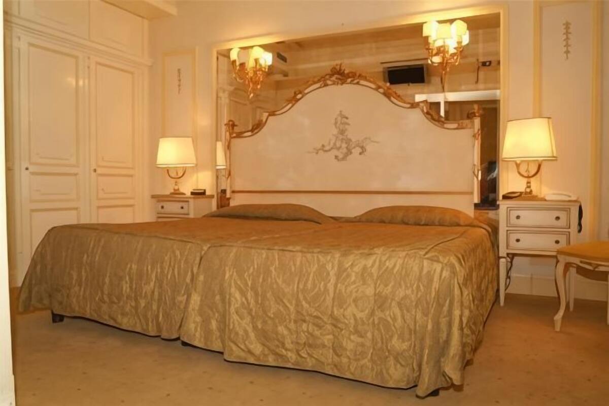 Un grand lit avec une tête de lit, deux tables de chevet avec des lampes et une chaise.