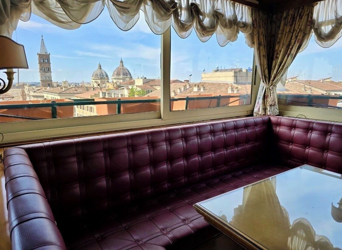 A room with a large window, a cushioned bench, and a table.