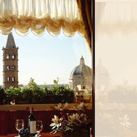 A table with a bottle of wine, a glass, and a vase of flowers, overlooking a cityscape with a tower and a dome.
