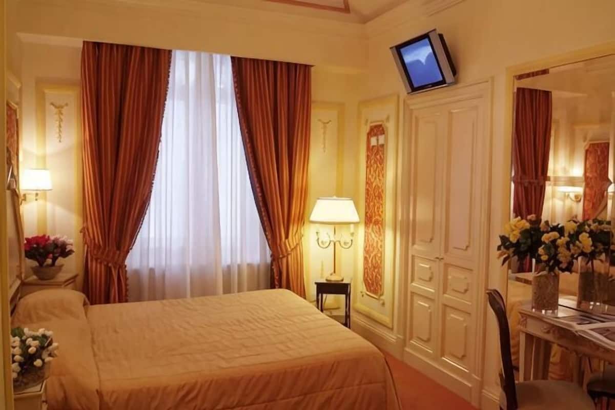 Une chambre d’hôtel avec un lit, un bureau, une chaise, une télévision et un miroir.