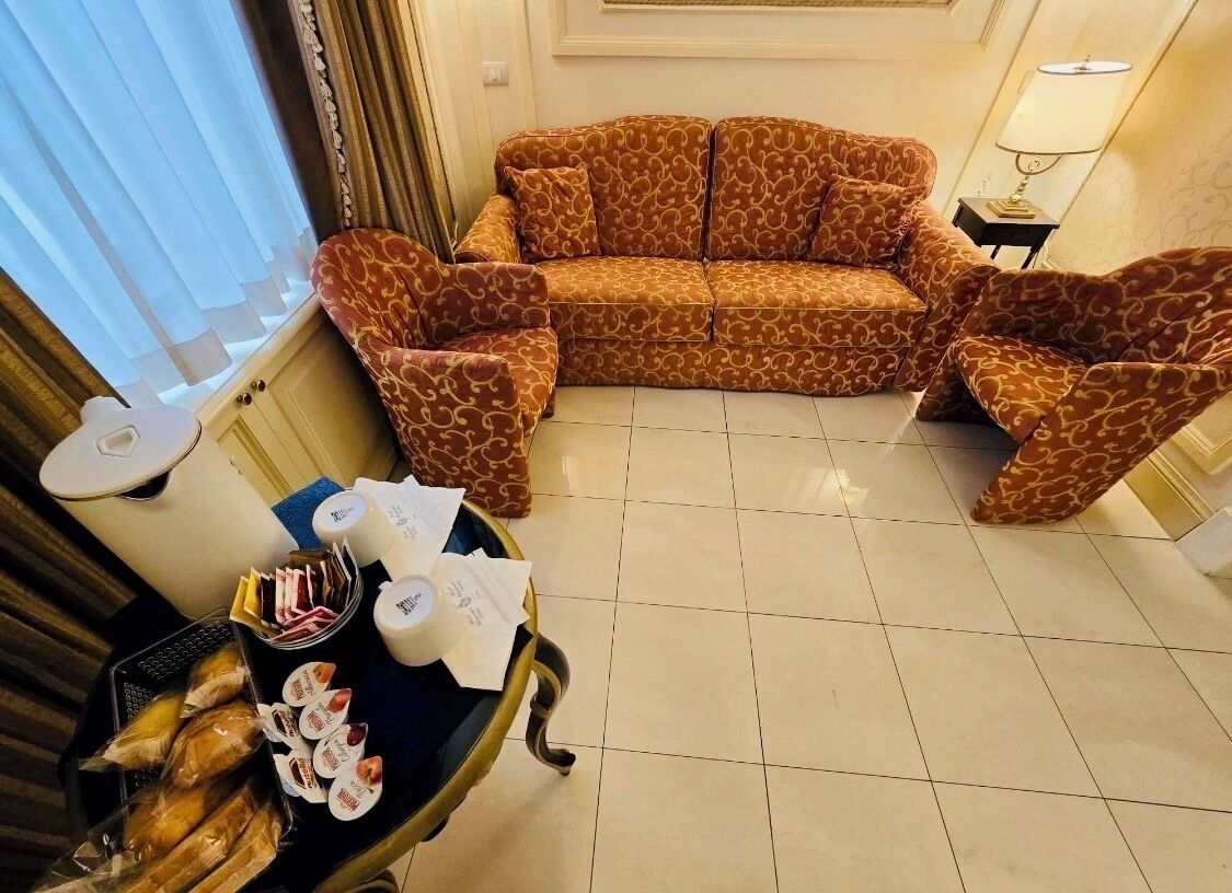 Un salón con un sofá estampado, una mesita auxiliar con una lámpara y una bandeja con comida y papeles.