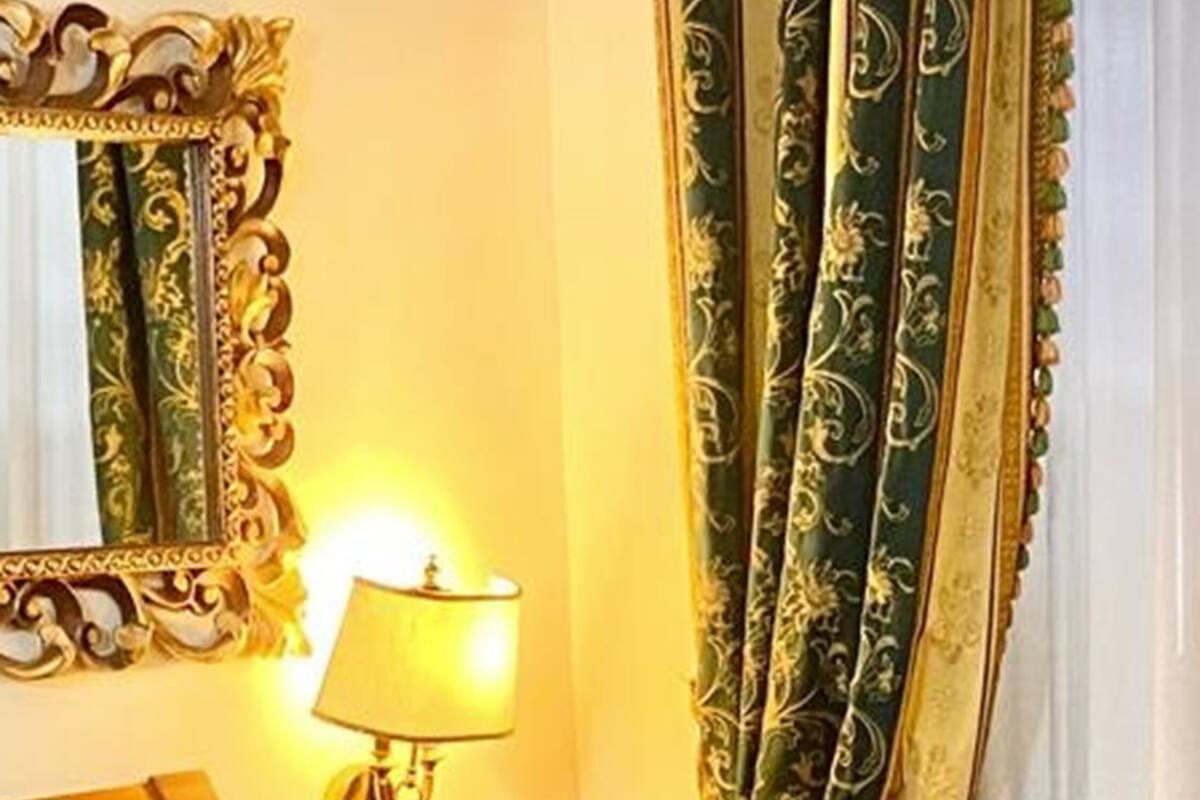 Une chambre d’hôtel avec un lit, une table de chevet, une lampe, un miroir et des rideaux.