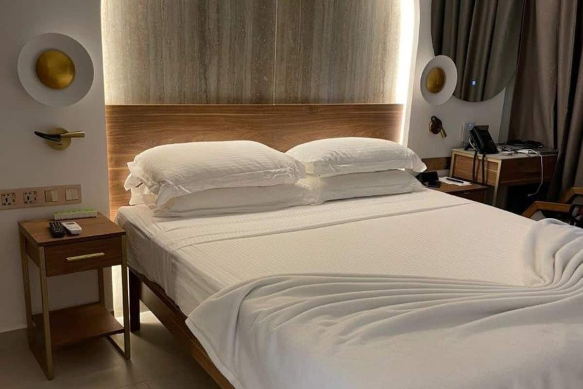 A modern hotel room with a large bed, a wooden headboard, and a round wall light.