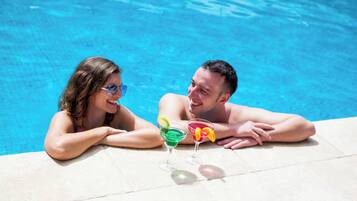 Dos personas descansando junto a una piscina con bebidas.