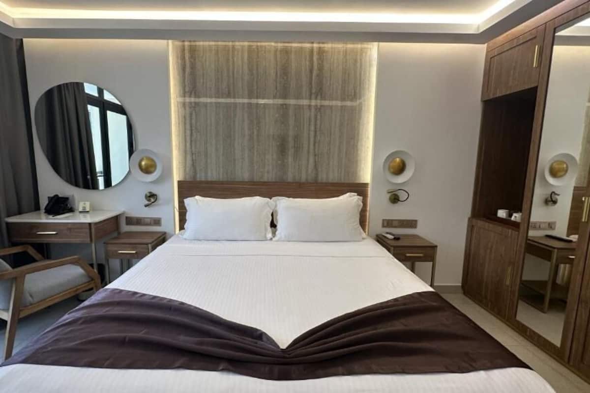 A hotel room with a large bed, a desk, a chair, a wardrobe, and a mirror.