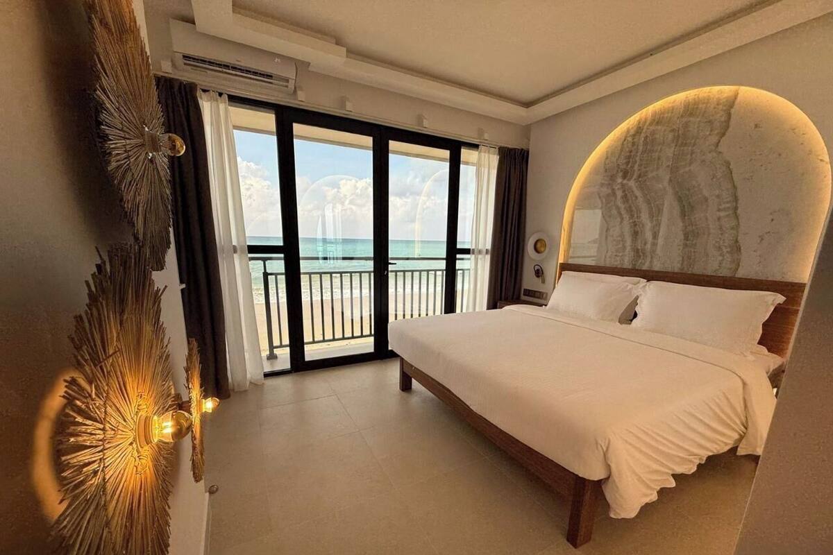 A bedroom with a large bed, a view of the ocean, and a balcony.