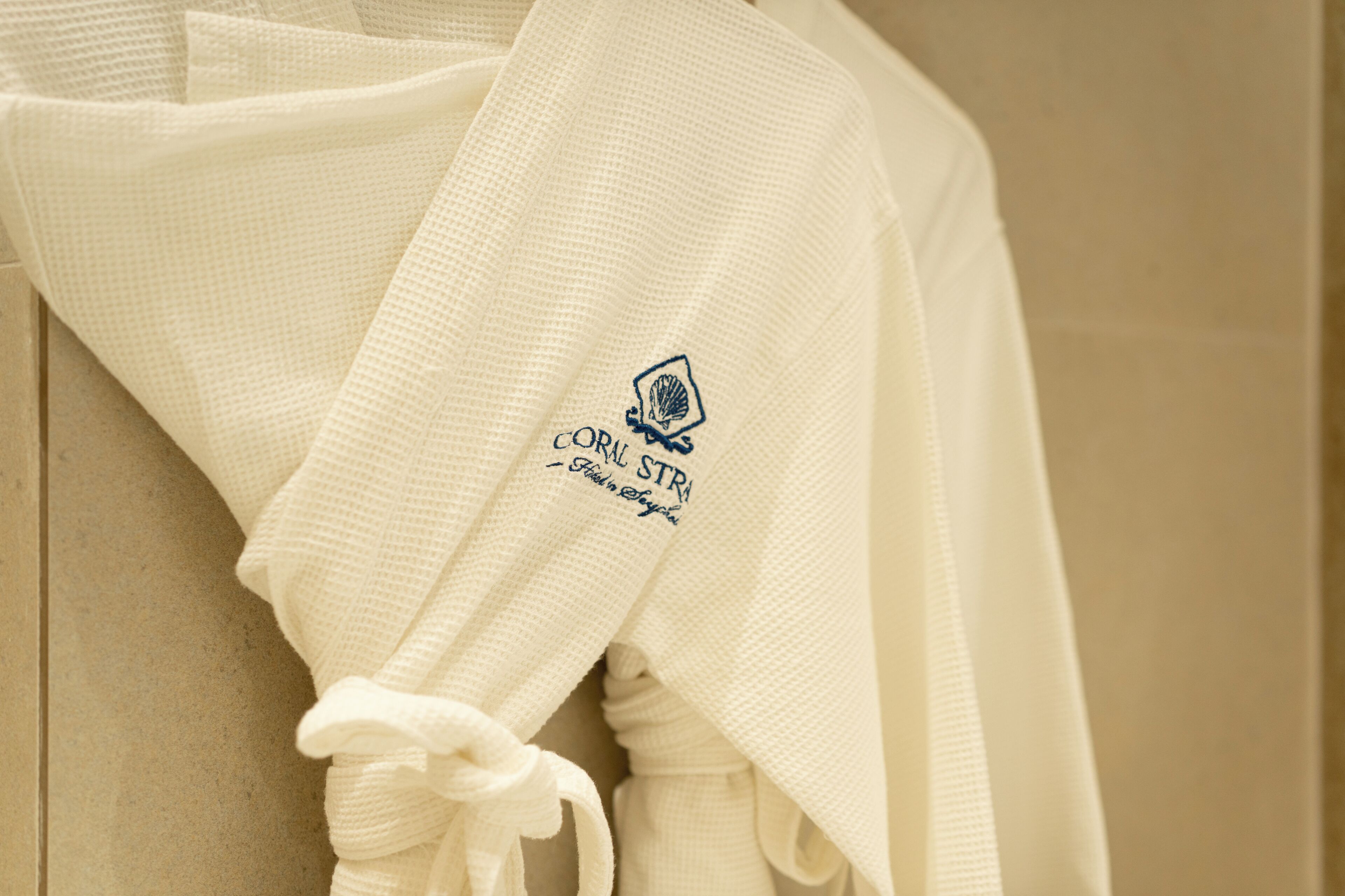 A white towel with a logo and text, hanging on a beige wall.