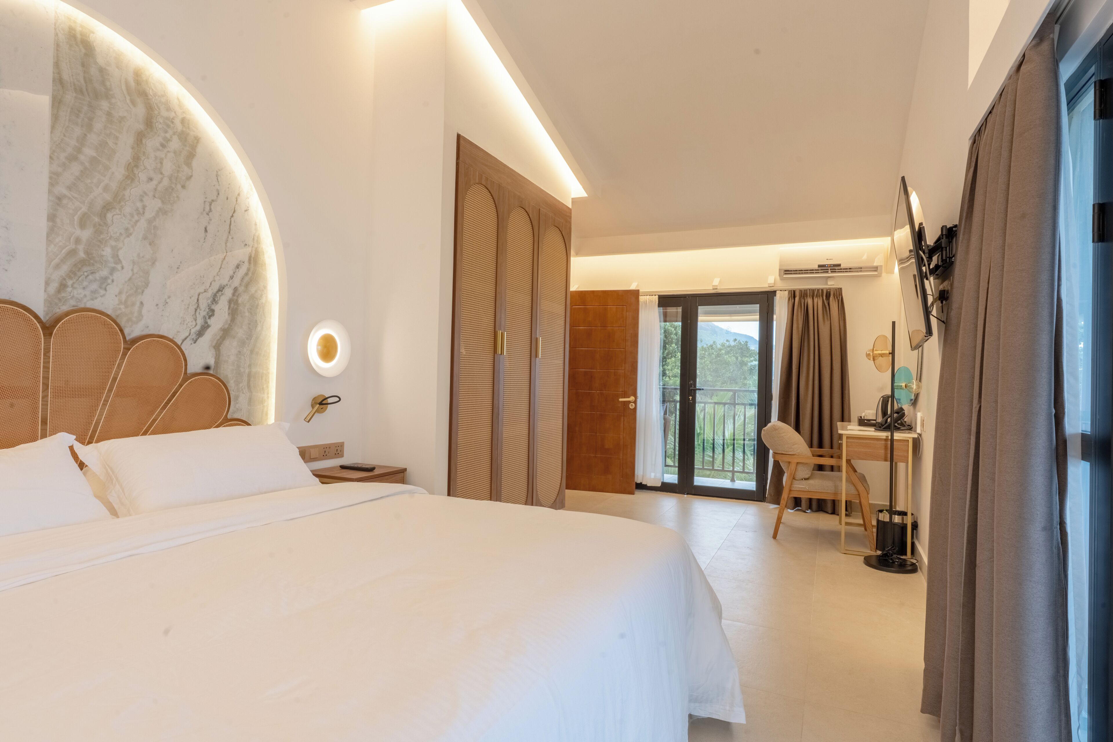 A modern hotel room with a large bed, a desk, and a balcony with curtains.
