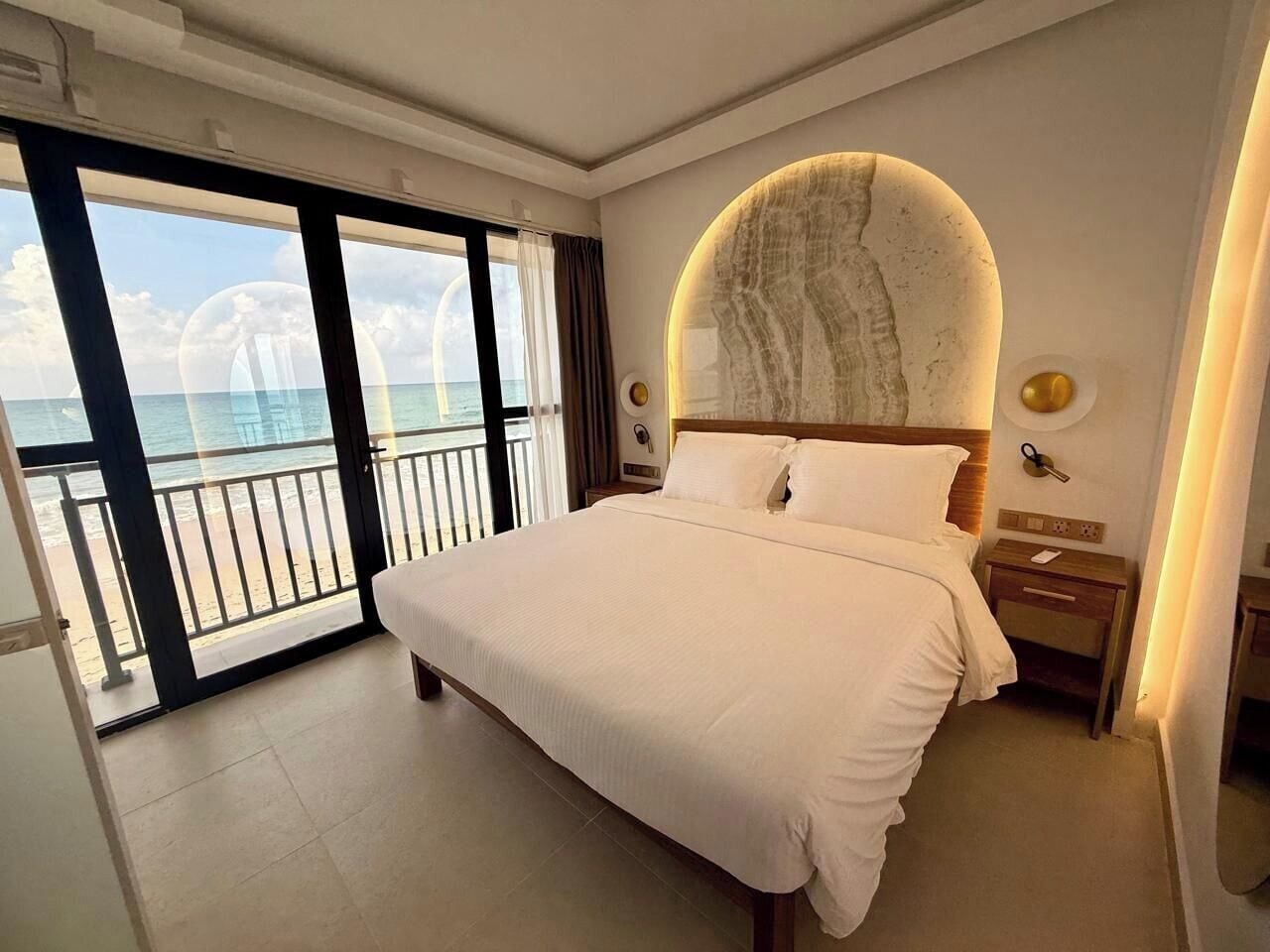 Habitación de hotel con una cama grande, vista al océano y un balcón.
