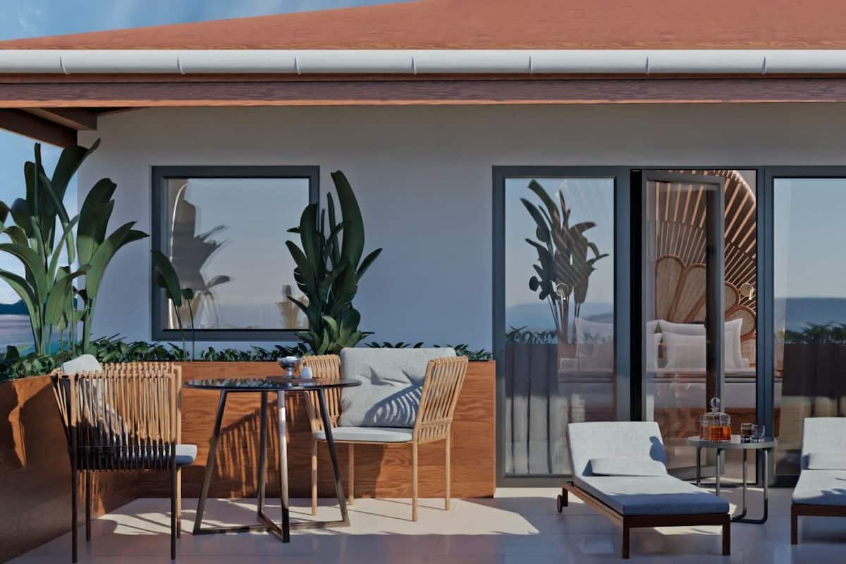 A modern outdoor patio with a dining set, lounge chairs, and large windows offering a view of the ocean.