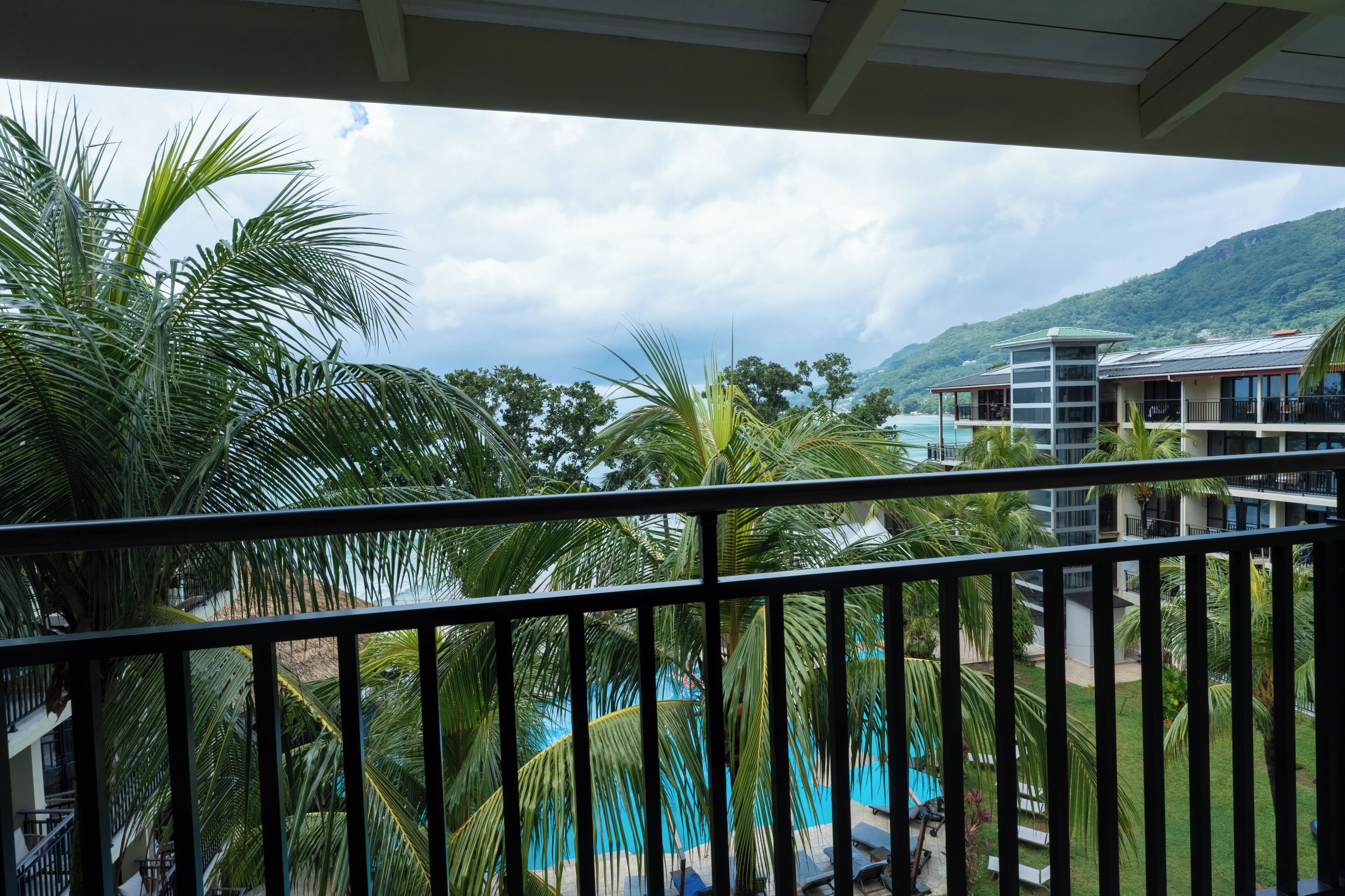 A balcony with a view of a pool, palm trees, and a building with a balcony.