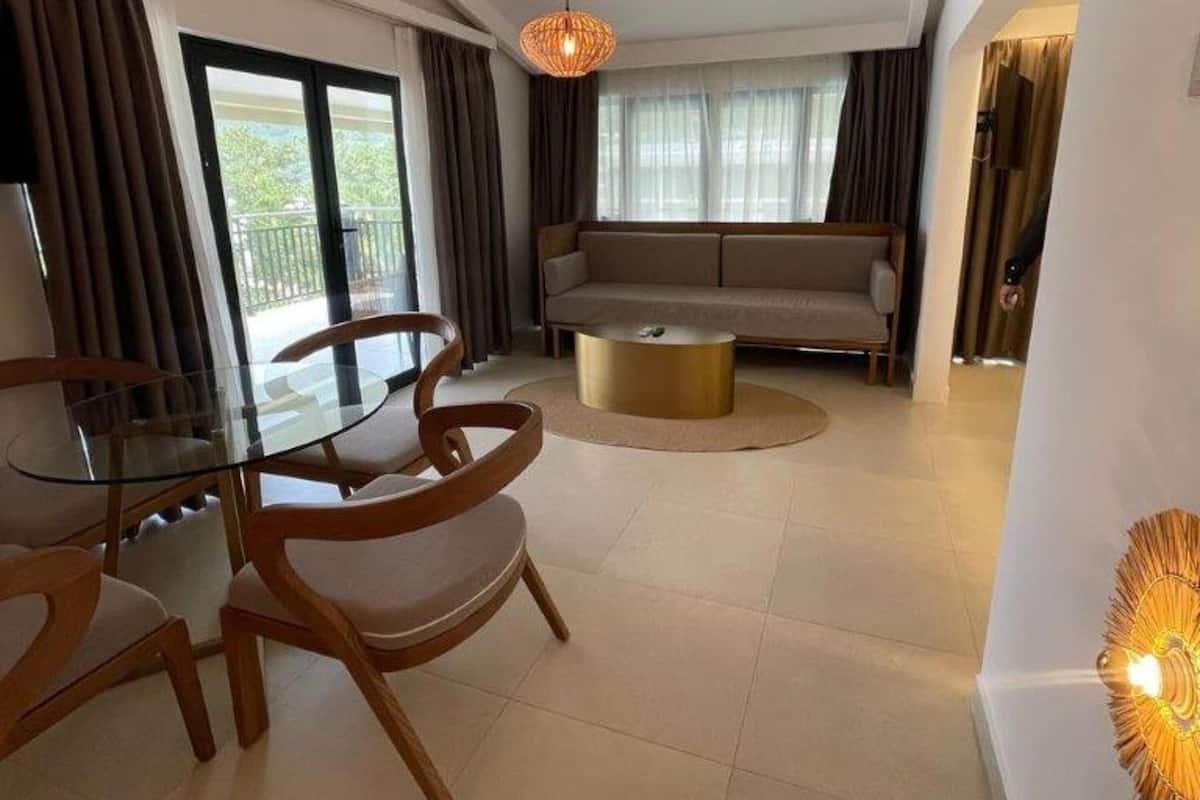 A modern living room with a glass dining table, wooden chairs, a round coffee table, a sofa, and a hanging light fixture.