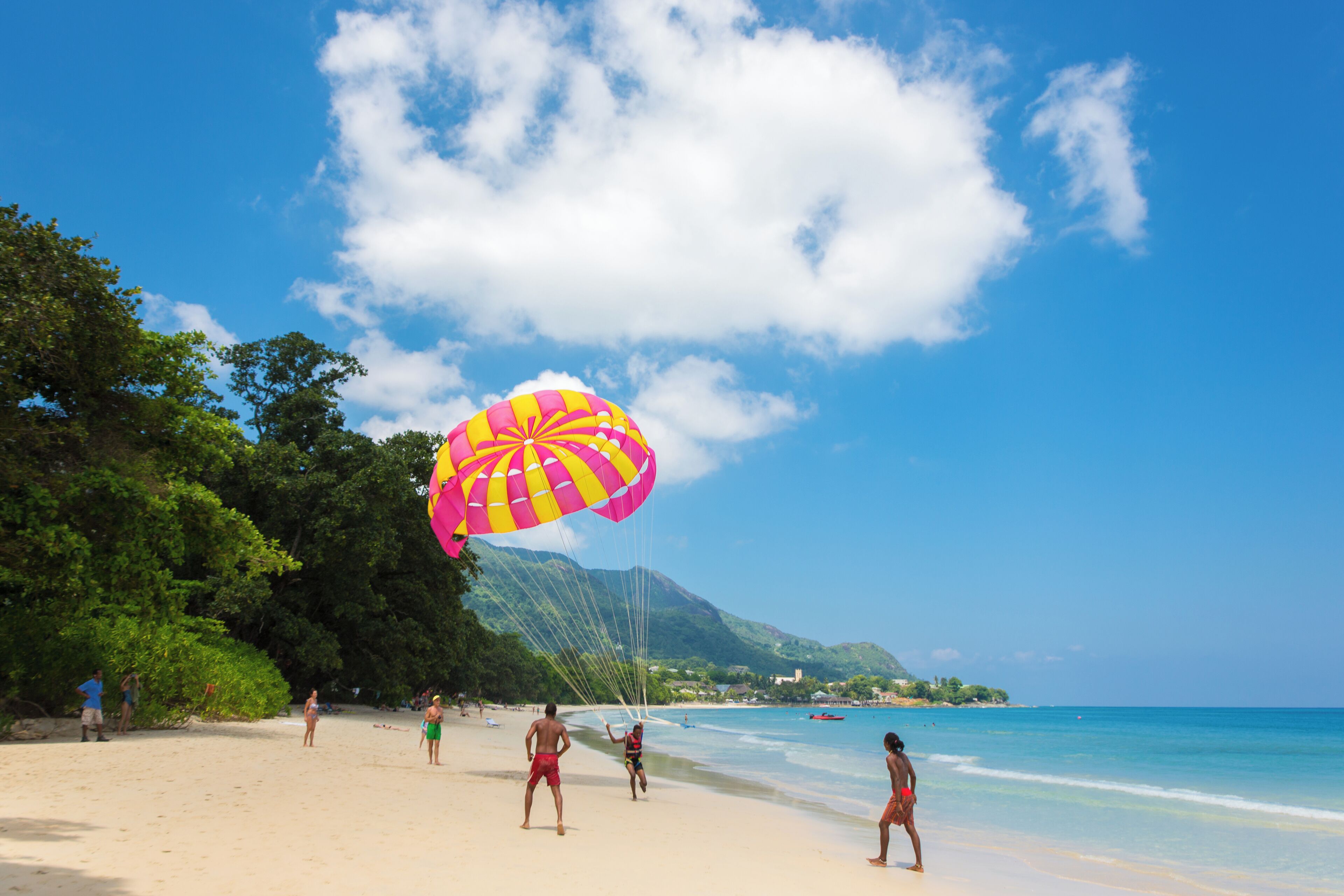 A beach with people, a colorful parasail, and clear blue skies.