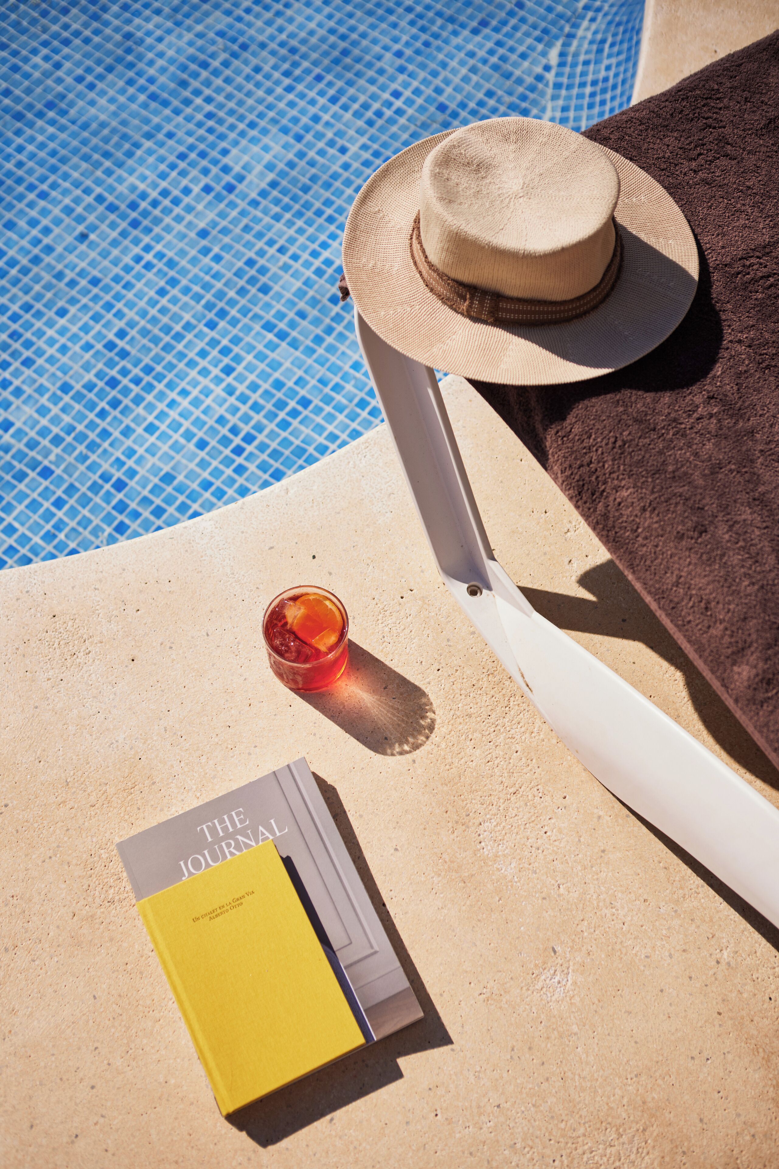 Una tumbona con sombrero y una bebida al lado de una piscina.